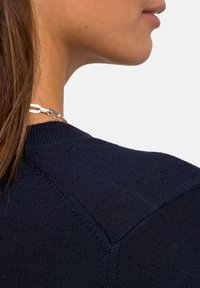 Marineblaues Strickpullover mit einem strukturierten Muster und einem runden Ausschnitt. Sichtbare Nahtdetails und eine Nahaufnahme der Stofftextur.