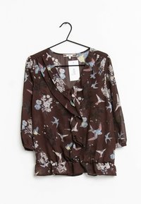 Brun blomstret bluse med indpakningsdesign, trekvart ærmer, volangkant og farverige fugle- og blomster mønstre. Hænger på en sort krog.