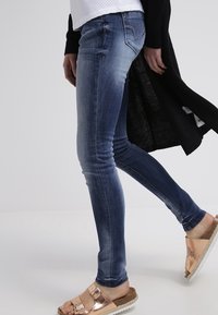 Blå denim skinny jeans med lätt blekning, med midjehöjd och klassisk femfickdesign, i kombination med sandaler i roséguld.