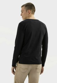 Langärmliges schwarzes T-Shirt mit rundem Ausschnitt und weicher Textur. Kombiniert mit hellbeigen Hosen mit Gesäßtaschen.