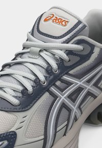 Artimos planas tamsiai mėlynos ir pilkos Asics bėgimo batų su baltais raišteliais ir tinklinio viršutine dalimi šone bei liežuvėlyje.