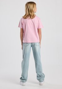 Camiseta de manga corta rosa claro combinada con jeans de mezclilla de pierna ancha azul claro y zapatillas blancas, vista desde la parte de atrás.