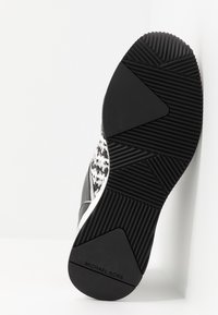 Semelle en caoutchouc noir avec adhérence texturée ; tige tissée avec un motif noir et blanc ; marqué « Michael Kors » à l'arrière.