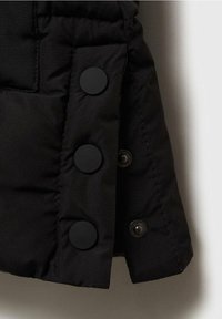 Detal puchowej czarnej kurtki z pikowaną teksturą, trzema dużymi czarnymi matowymi guzikami i zatrzaskiem po jednej stronie.