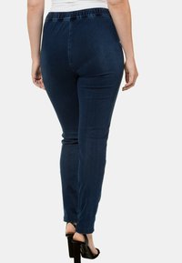 Pantalones de mezclilla azul oscuro con una textura suave, cinturilla elástica y corte ajustado, con un diseño hasta el tobillo y sin herrajes visibles.