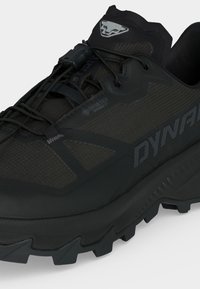 Chaussure outdoor noire Dynafit avec semelle robuste, système de laçage rapide, tissu Gore-Tex et logo d'une tête de puma sur la languette.