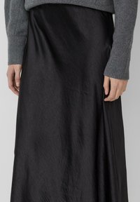 Zwarte, satijnachtige rok met een gladde textuur en een vloeiende ontwerp, gecombineerd met een grijze, ribbelgebreide trui bij de hand en pols.