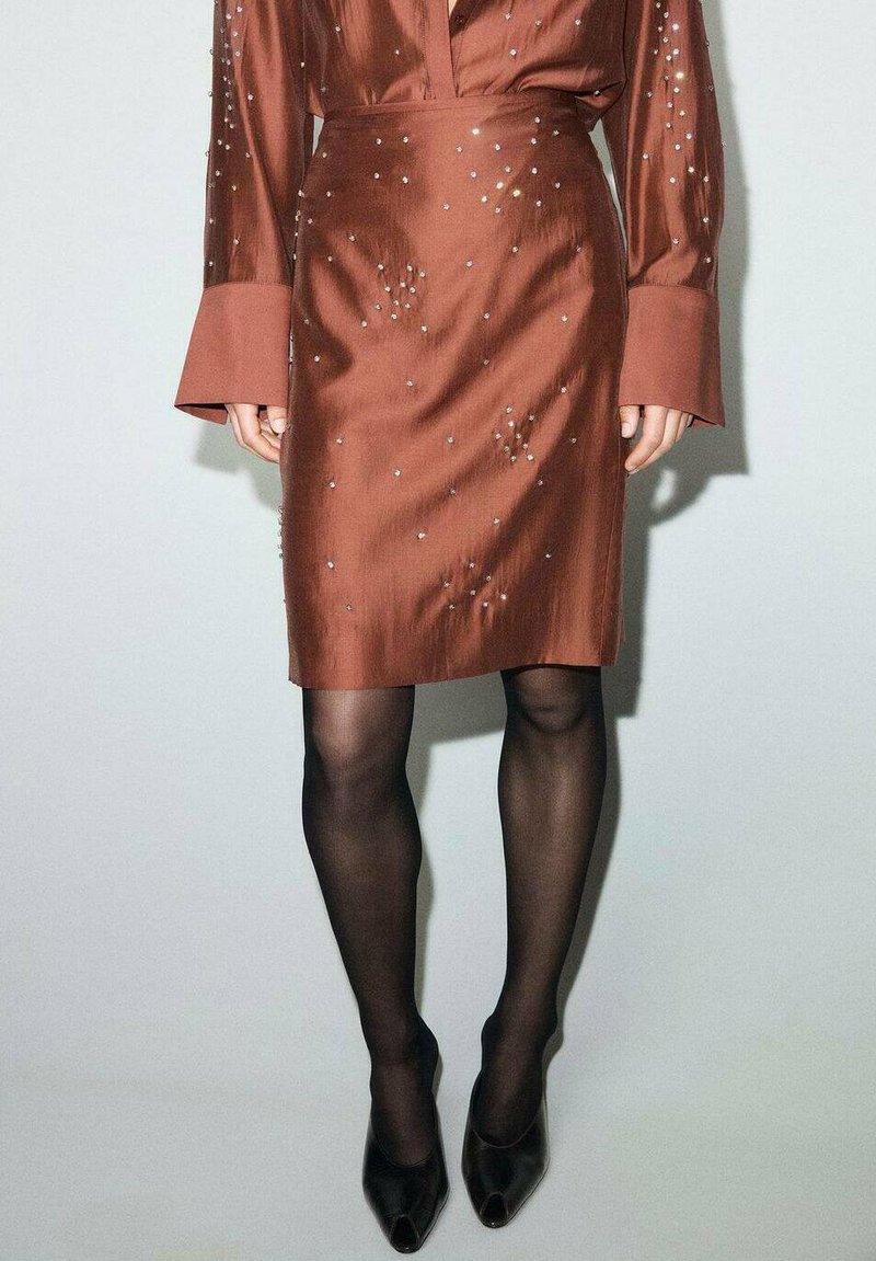 Brauer Satinrock mit enger Silhouette, verziert mit verstreuten Strasssteinen, kombiniert mit schwarzen, transparenten Strumpfhosen und schwarzen, offenen High Heels.