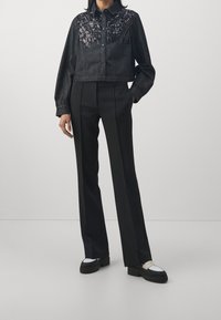 Giubbotto di jeans cropped nero con dettagli in paillettes sulle spalle, abbinato a pantaloni neri a vita alta e scarpe con plateau con accenti bianchi.