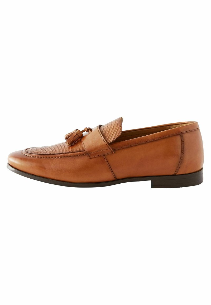 Mocassin en cuir brun sans lacets avec un panneau texturé et un détail de pompon, présentant un bout rond et une semelle plate.