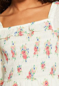 Vestido blanco de flores con detalles de fruncido. Presenta flores rosas y azules, cuello con volantes y tela texturizada.