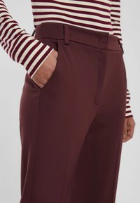 Pantaloni bordeaux su misura con una texture liscia, dotati di tasche laterali e un fit snello, abbinati a una maglietta a righe a maniche lunghe.