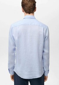 Lichtblauw shirt met lange mouwen en een subtiele structuur, voorzien van een klassieke kraag, knoopmanchetten en een afgeronde zoom aan de achterkant.
