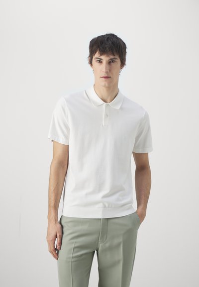 Hvit kortermet polo skjorte med klassisk krage, teksturert stoff og to-knapps placket, sammen med lys grønne skräddersydde bukser.