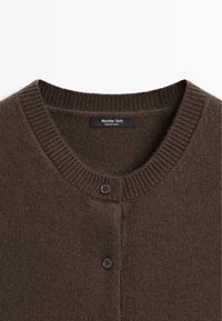 Cardigan en tricot marron avec un col côtelé, deux boutons noirs et une texture lisse. L'étiquette indique "Massimo Dutti, fabriqué en Chine."