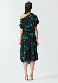 Crna haljina s šarenim zelenim i ljubičastim cvjetnim uzorcima, s drapiranim jednim ramenom, naboranim detaljem u struku, lepršavim suknjom, srebrnim potpeticama.