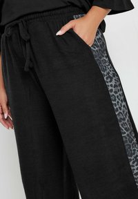 Czarne dresy z miękkiego materiału, z boku ozdobione panelami w leoparda, posiadające elastyczny pas z troczkiem. Zawierają kieszenie.