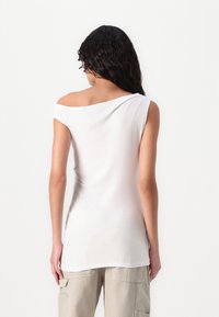 Haut blanc à épaules dénudées en tissu doux et léger, avec des manches courtes et une coupe décontractée, associé à un pantalon cargo beige.