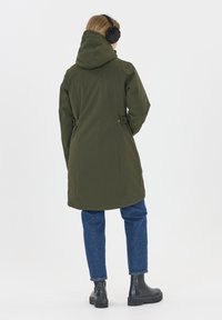 Olijfgroene waterdichte parka met capuchon, verstelbare taille en drukknoopdetails. G gedragen over blauwe jeans en zwarte enkellaarsjes, met een eenvoudig ontwerp.