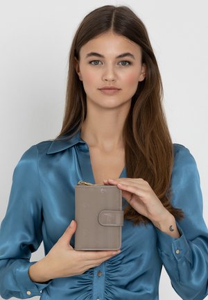 Gray leather wallet with embossed detailing, zip closure, and a snap-button flap. held by a model in a blue satin shirt.