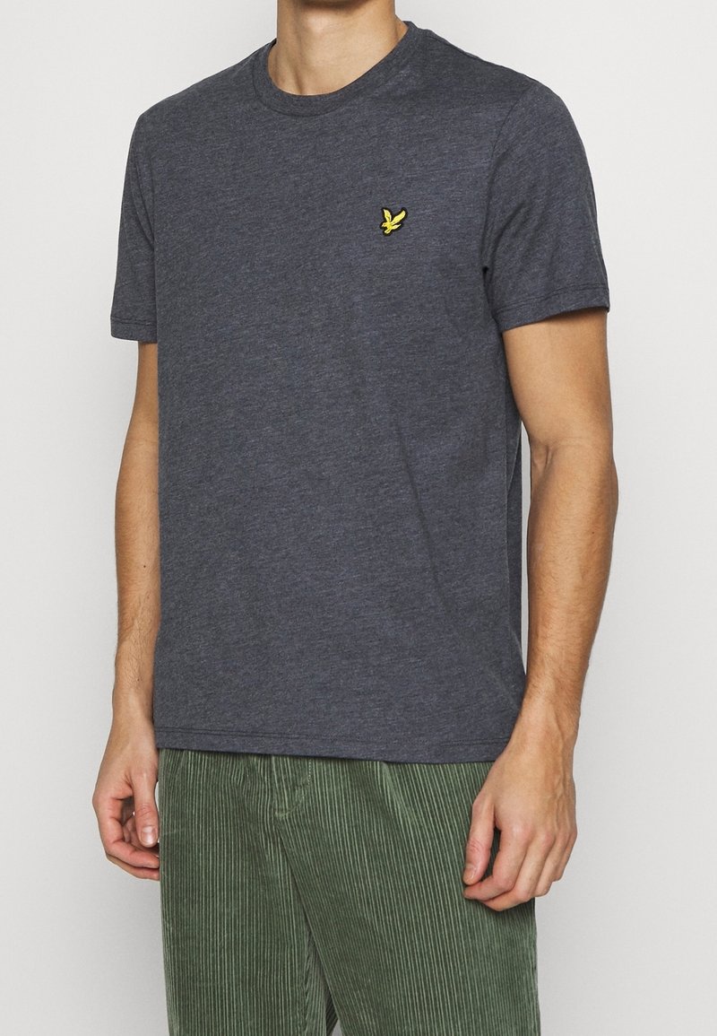 T-shirt a maniche corte grigio scuro realizzato in tessuto morbido, con un piccolo logo di un uccellino giallo sul lato sinistro del petto. Vestibilità casual e design a girocollo.