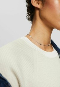 Sølvring med små geometriske accenter, båret med en ribbet hvid sweater. Glat tekstur, delikat kæde design.
