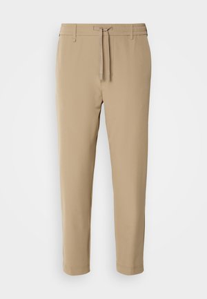 Beige, tapered pants with an elastic waistband and drawstring. Smooth fabric with a clean design and no visible patterns or hardware.