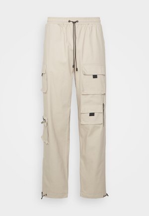 Pantaloni cargo beige con vita elasticizzata e cordoncino, dotati di più tasche, zip e polsini regolabili all'orlo.