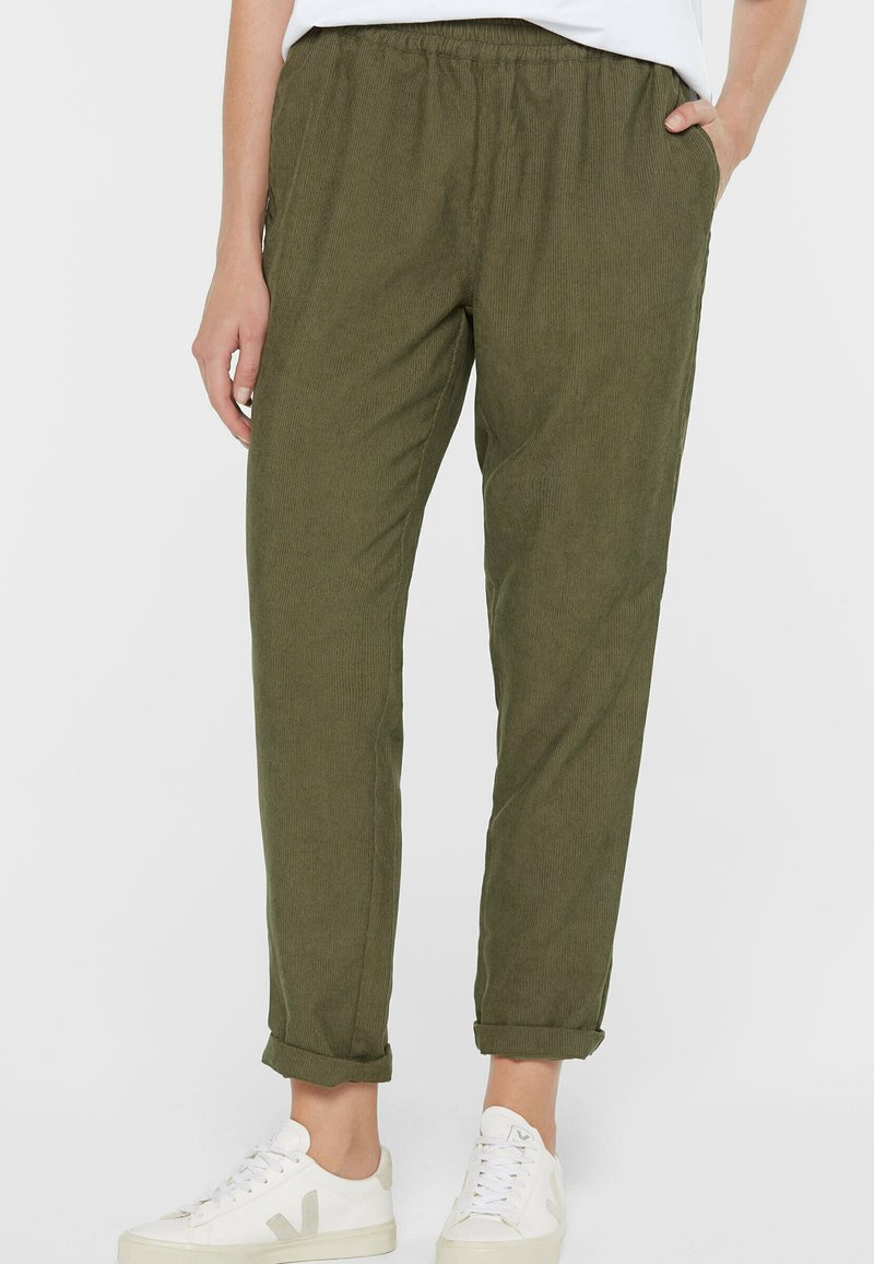 Olive green, ribbed, elastic waistband trousers with side pockets, tapered ankle length, paired with white sneakers.
