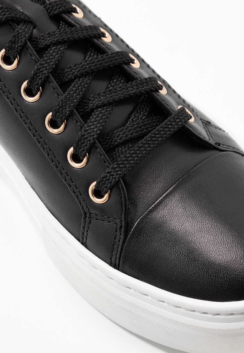 Schwarze Ledersneaker mit texturierter Oberfläche, ausgestattet mit goldenen Ösen, schwarzen Schnürsenkeln und einer weißen Gummisohle. Rundes Zehen-Design.