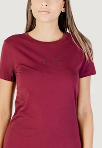 T-shirt corto bordeaux in morbido cotone, con logo "A|X" in accenti brillanti sul davanti. Tessuto liscio e vestibilità classica.
