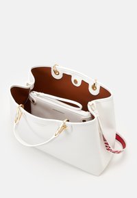 Witte leren totebag met een bruin interieur, voorzien van gouden accenten, een zak met rits en een patroonriem. Open bovenkant ontwerp.