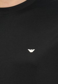 Zwart katoenen T-shirt met ronde hals en een klein, wit geborduurd logo op de borst, met een gladde, zachte textuur.