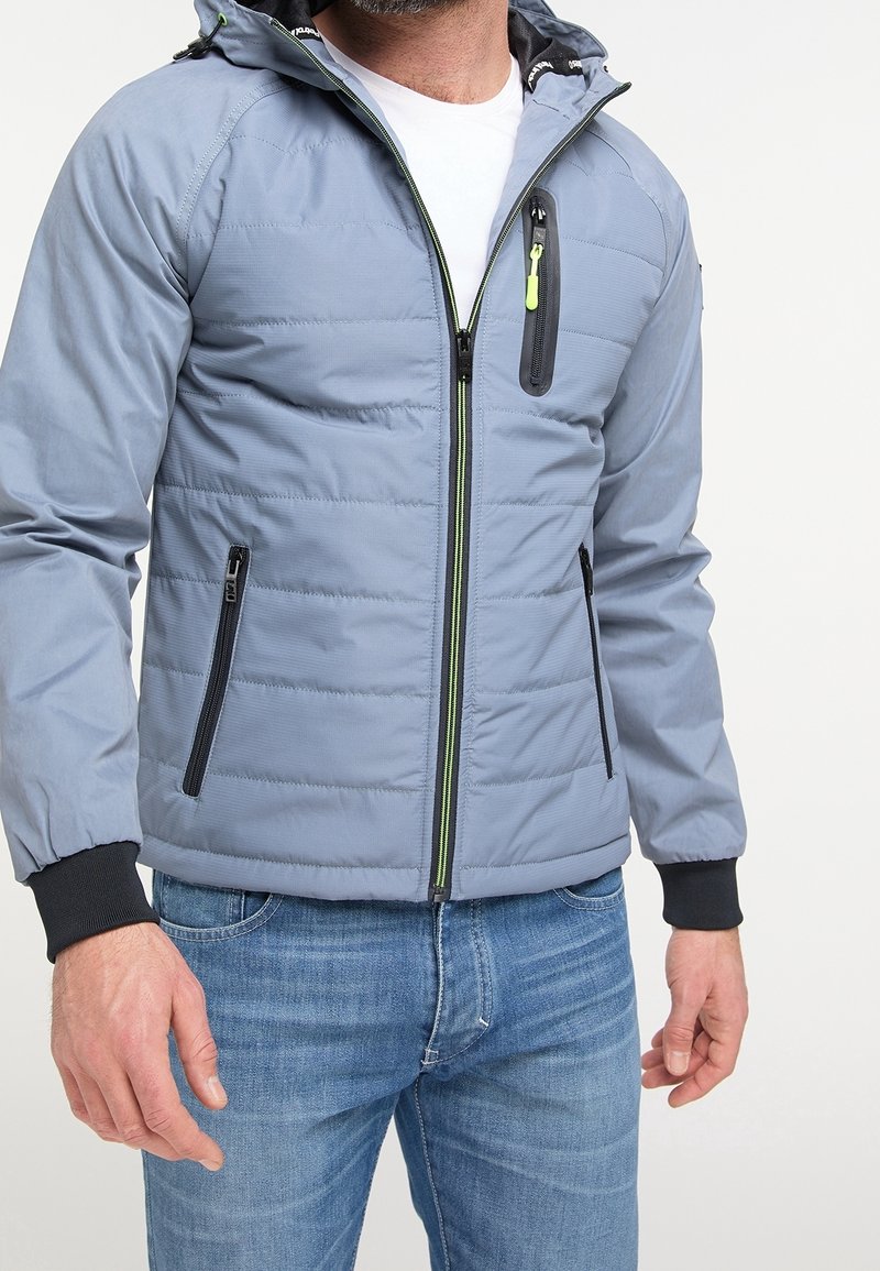 Jasnoniebieska kurtka ocieplana z kapturem, z czarnymi zamkami błyskawicznymi i mankietami, zielonymi akcentami zamków oraz pikowanym wzorem.