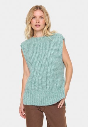 Haut sans manches en tricot teal clair avec un motif texturé, encolure ronde et ourlet côtelé. Porté avec un pantalon marron.