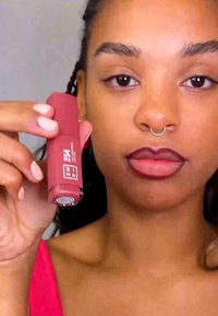 Lepper i en sylinderformet, matt mauve beholder med sølvdetaljer. Merket viser nyansen "254" og merkevarenavn. Glatt tekstur synlig.