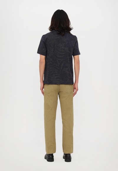 Tricou gri închis cu mâneci scurte, cu un model texturat subtil. Purtați-l cu pantaloni bej deschis, cu un model asemănător șarpelui, și cu pantofi negri.