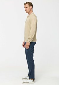 Polo shirt bej cu mâneci lungi prezintă un guler clasic. Este asortat cu pantaloni navy și adidași albi cu accente gri.