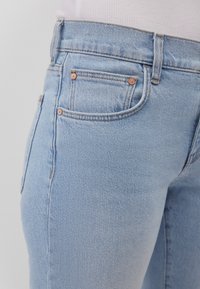 Light blue denim jeans with a high waist, featuring back pockets, copper rivet detailing, and a smooth texture.
