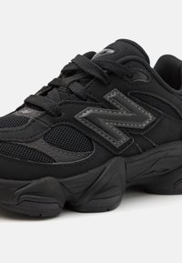 Chaussure de sport noire avec tige en mesh et synthétique. Présente un col rembourré, un système de laçage et une semelle intermédiaire texturée. Affiche un logo bien en vue.