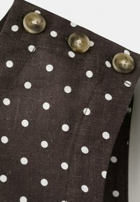 Czarna tkanina w białe kropki z trzema dużymi półprzezroczystymi brązowymi guzikami ułożonymi wzdłuż krawędzi szwu.
