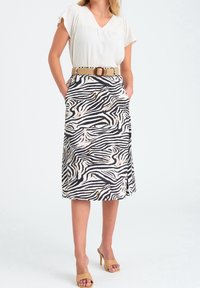 Kvinna som bär en beige kortärmad blus inskjuten i en midiklänning med zebramönster, med ett vävt beige bälte och bruna högklackade sandaler.