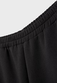 Nærbillede af sort elastisk linning på bukser af blødt stof med detalje af rynket syning.