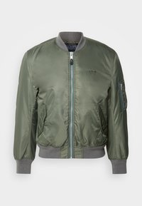 Veste bomber vert olive avec une finition lisse et brillante. Elle possède un col et des poignets côtelés gris, une fermeture éclair sur le devant, et une poche sur la manche.