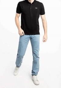 Czarny polo z kołnierzykiem i białym logo, zestawiony z jasnoniebieskimi dżinsami i białymi sneakersami. Ubranie ma casualowy styl.