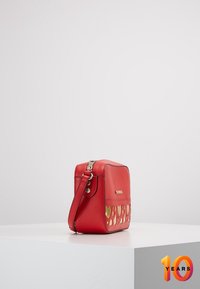 Borsa a tracolla rossa in pelle con motivo a cuore ritagliato, dettagli dorati, forma rettangolare, chiusura con zip e spallaccio regolabile.