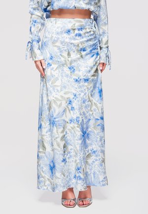 Gonna maxi bianca fluida con motivo floreale blu e grigio indossata con top corto abbinato e décolleté argento con punta aperta.