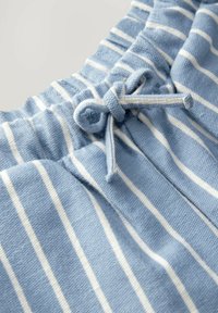Tissu bleu clair avec des rayures horizontales blanches, présentant une boucle de cordon nouée à la ceinture froncée d'un vêtement.