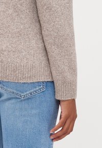 Maglione beige a maglia con orlo e polsini a coste, abbinato a jeans in denim azzurro chiaro, che mostrano una texture liscia e un design aderente.