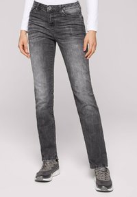 Jeans de mezclilla gris con un corte recto, que cuentan con cinco bolsillos y un sutil efecto de desgaste. Combinados con zapatillas grises y una camiseta de manga larga blanca.